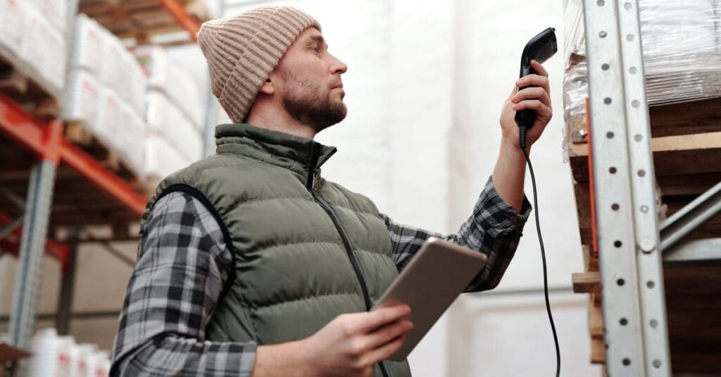 Male warehouse staff scanning inventory with handheld scanner and tablet indoors.